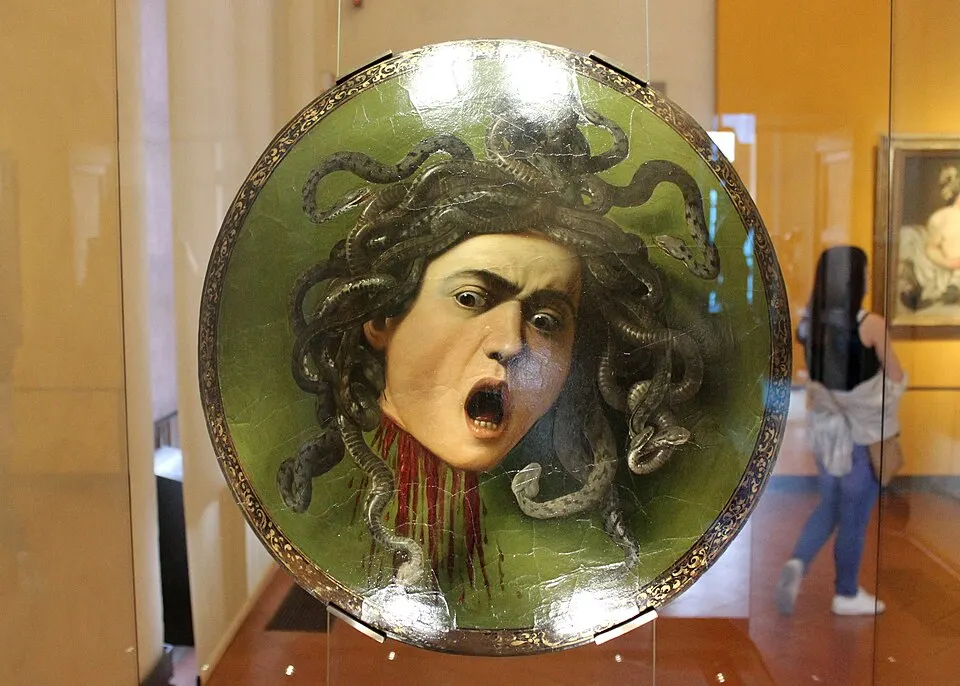 A round painted shield showing a screaming face with writhing snakes for hair on a green background.