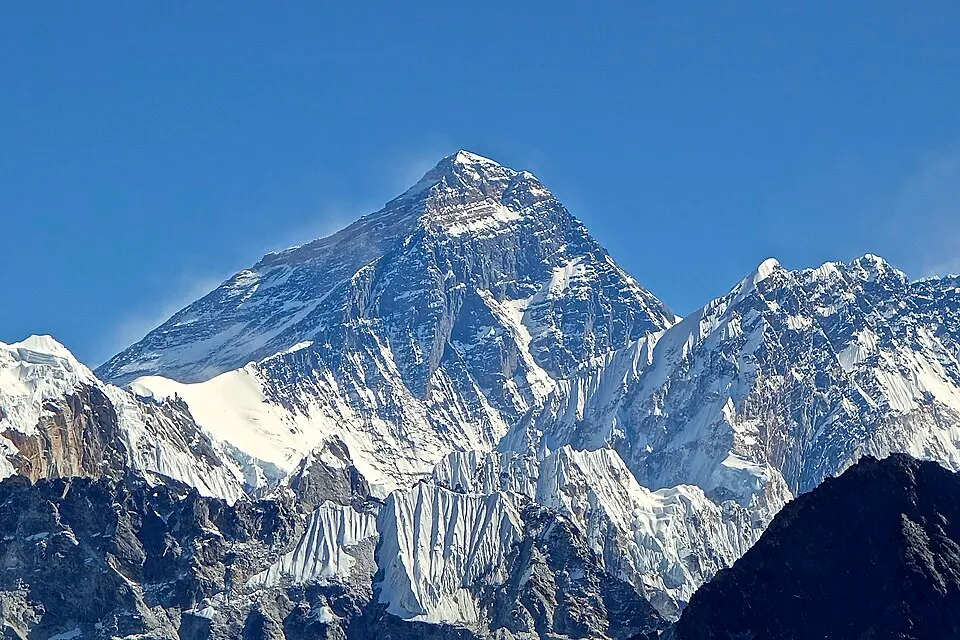 A steep snow-streaked rocky mountain peak against a clear blue sky.