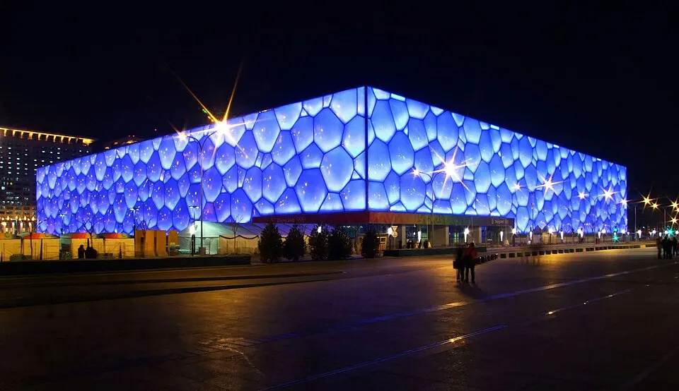 A glowing blue building covered in bubble-shaped panels, lit up at night.