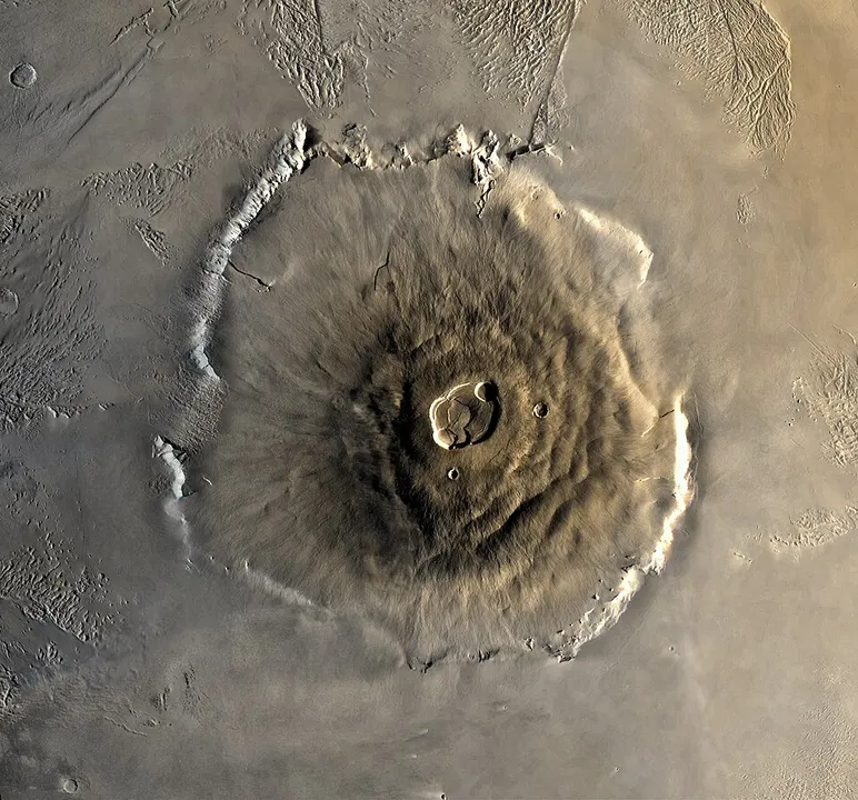 A giant rust-coloured shield volcano seen from orbit, with a wide cliff-ringed base.