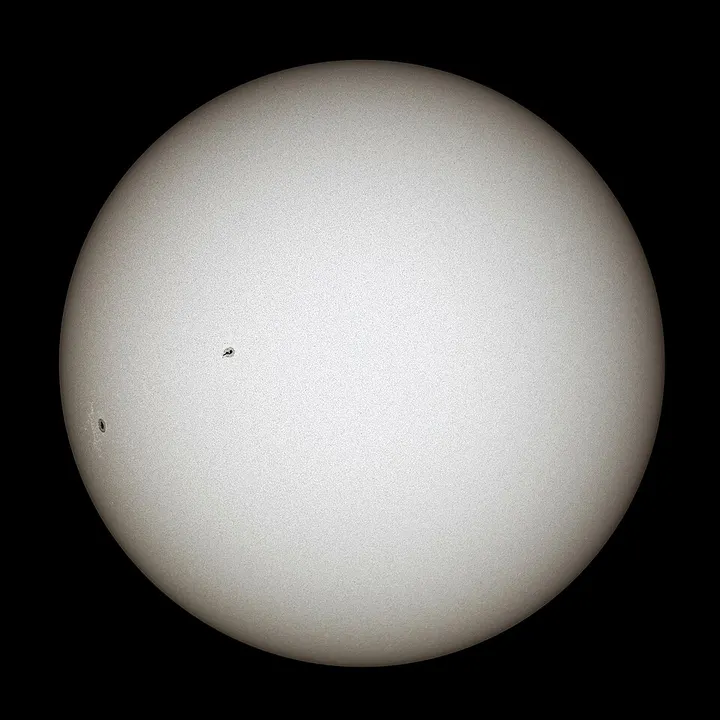 A bright white disc with a couple of small dark spots, against black space.