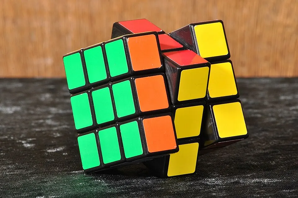 A colourful six-sided puzzle cube with green, orange, yellow and red squares, partly twisted out of alignment.