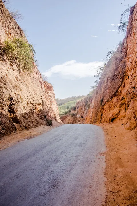 A paved road runs between two tall, steep walls of orange-red earth under a pale sky.