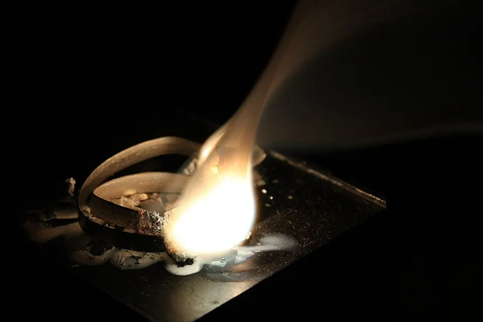 A thin metal ribbon burning with a very bright white flame in a dark room.