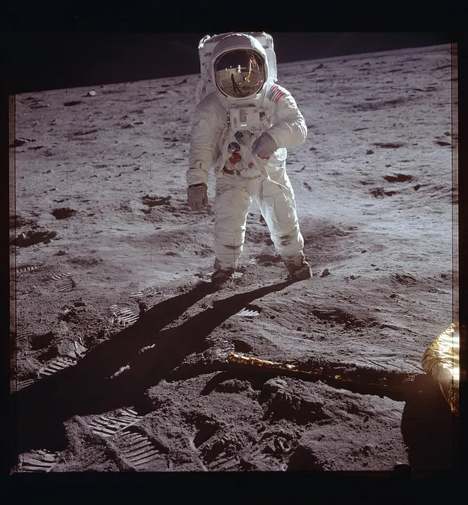 An astronaut in a white spacesuit standing on grey, dusty ground covered in footprints.