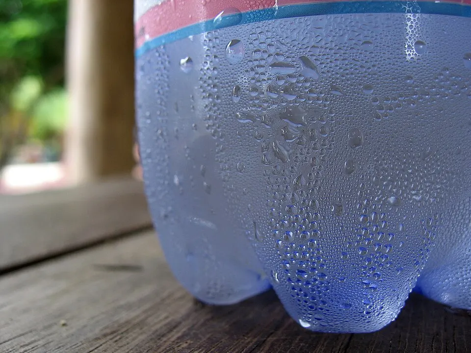 Close-up of a cold plastic bottle covered in tiny beads of water on a wooden table.