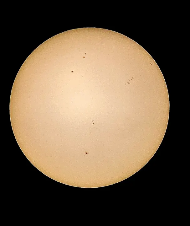 A round, pale-orange disc of the Sun against black sky with a few small dark spots on it.
