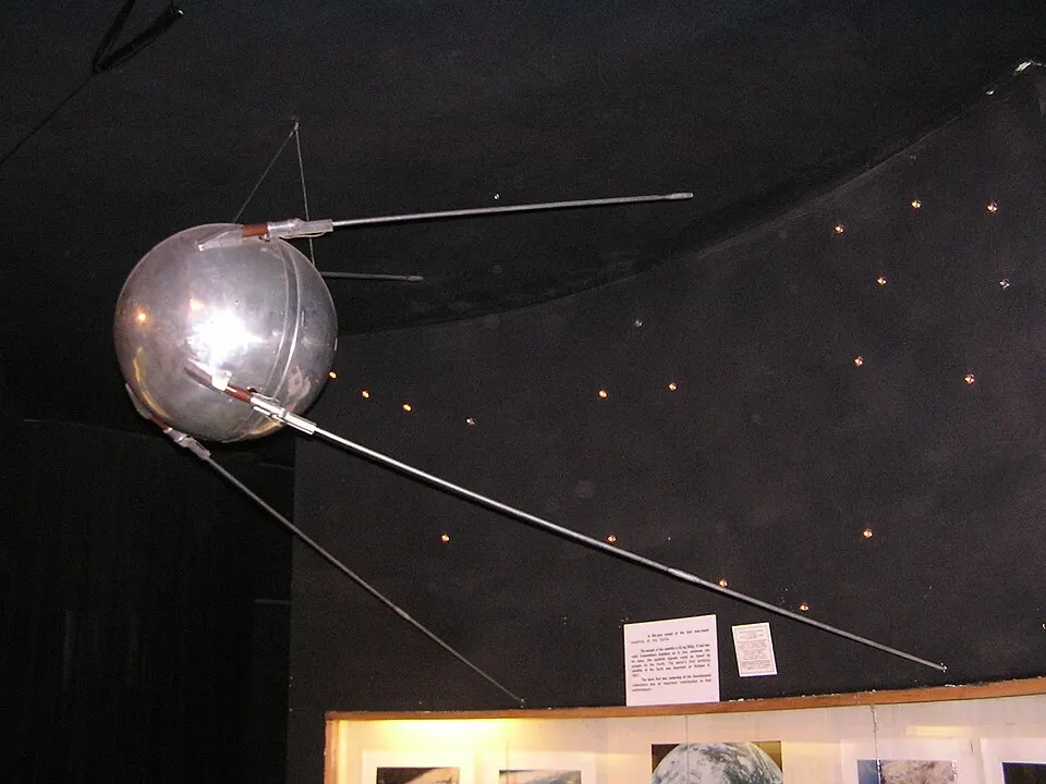 A polished metal sphere with four long thin antennas.