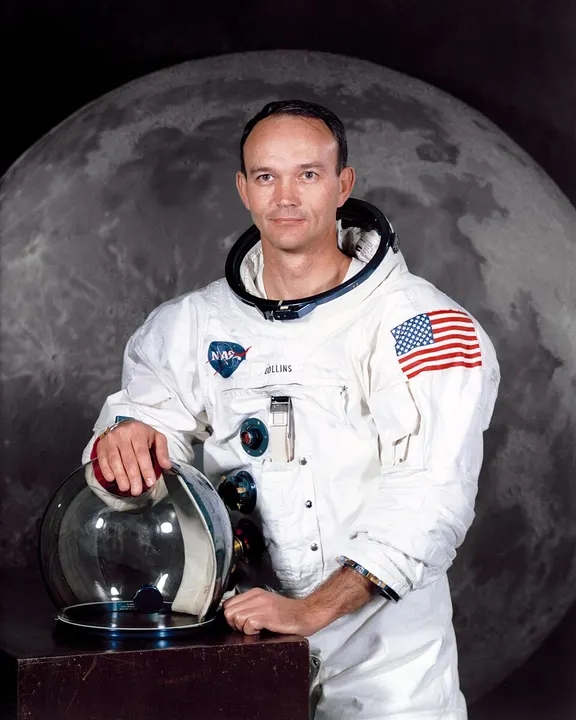 An astronaut in a white spacesuit holding a helmet.