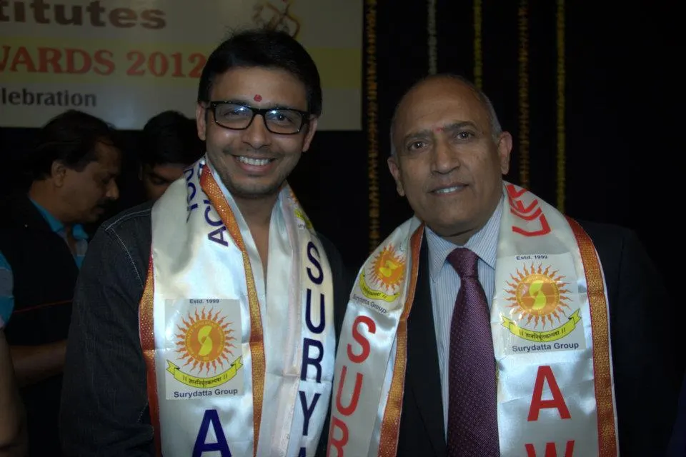 Two smiling men wearing ceremonial scarves at an awards event.