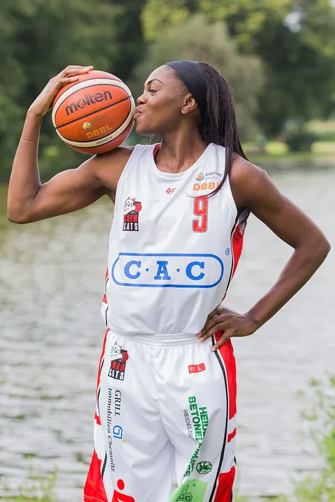 A basketball player in a white jersey kisses a ball while standing in front of a lake.