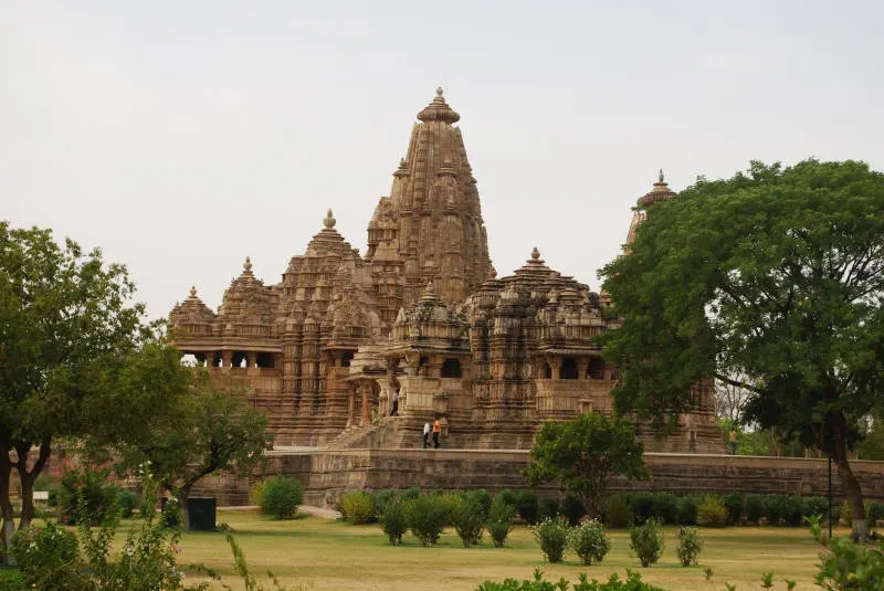A tall ancient sandstone temple with a stack of carved spires rising above a green garden.