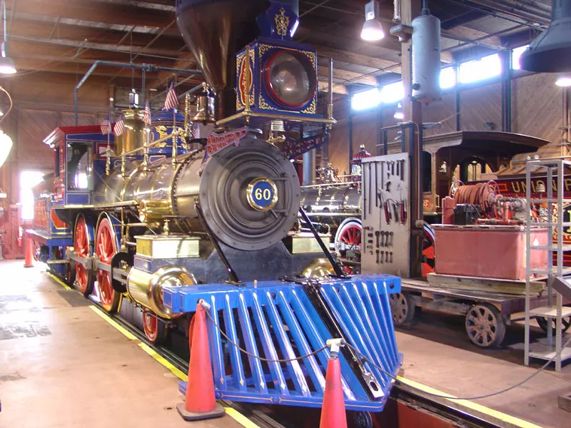 A brightly painted 19th-century steam locomotive numbered 60 with a blue cowcatcher, inside a railway shed.