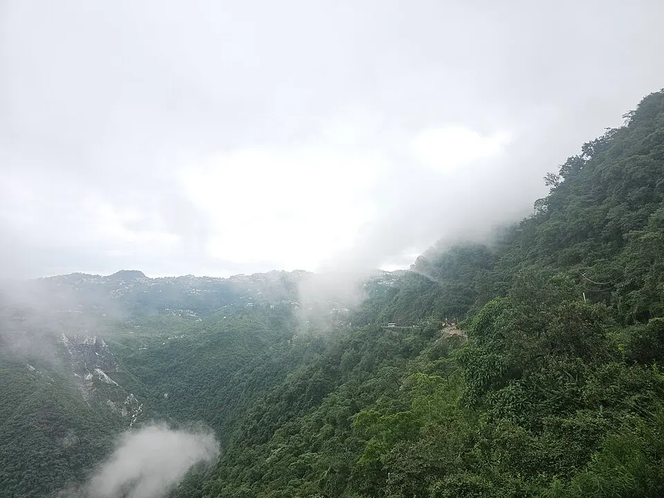 Green forested hillsides drop into a misty valley, with a hill town on the far ridge.