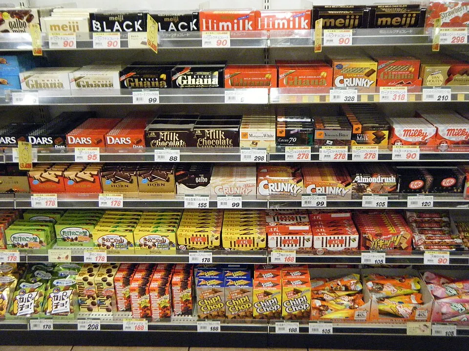 Supermarket shelves stacked with boxes of chocolate bars and snacks in bright wrappers with Japanese price tags.