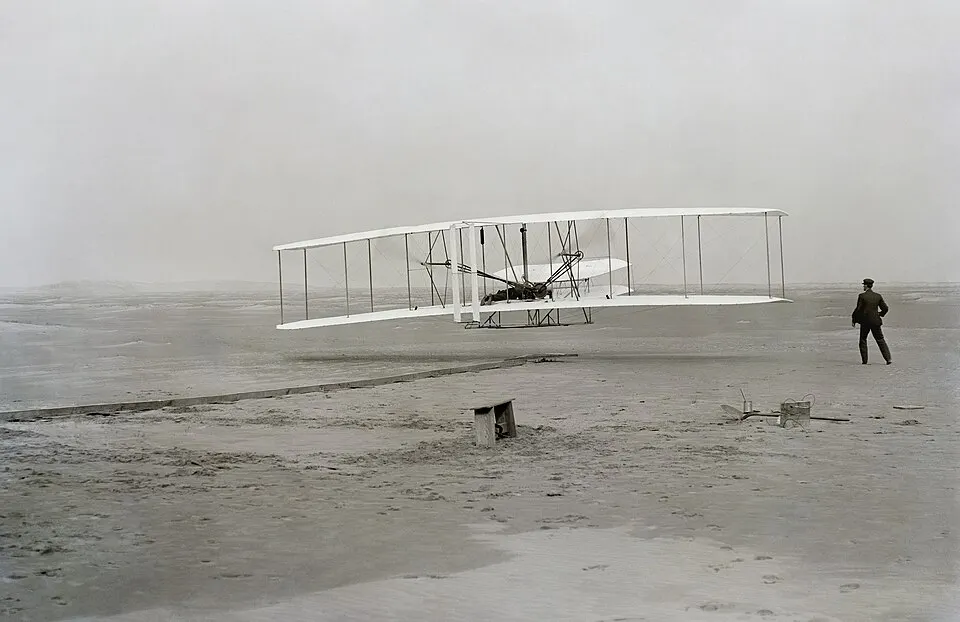 An early biplane flying just above a sandy beach.