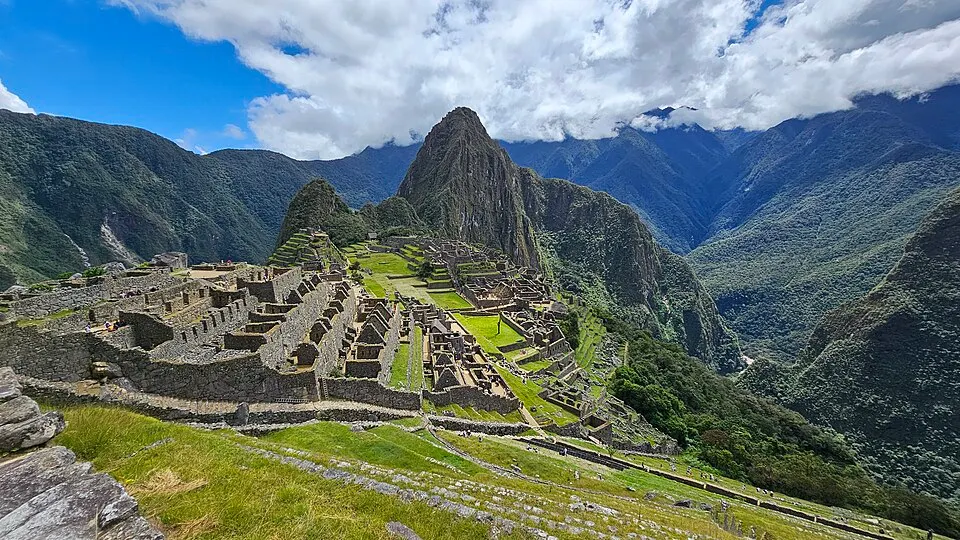 Ancient stone terraces and ruins on a green mountain ridge among steep peaks.