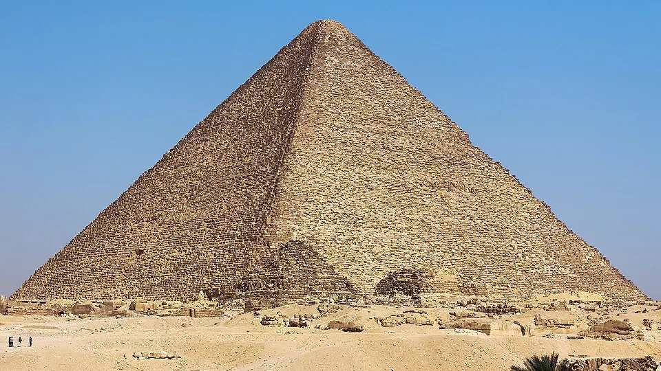 A huge stone pyramid rising from a desert plateau under a clear sky.