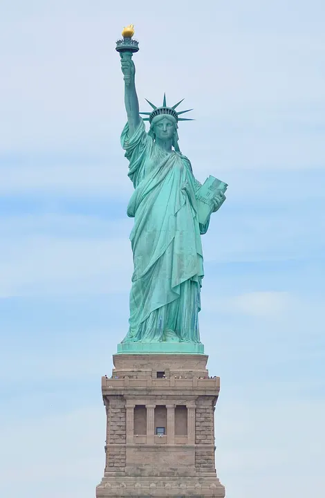 A green copper statue of a robed woman holding a torch high on an island pedestal.