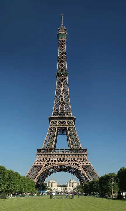 A tall wrought-iron lattice tower rising over a city park.