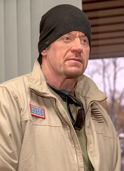 A tall wrestler in dark clothing and a hat.